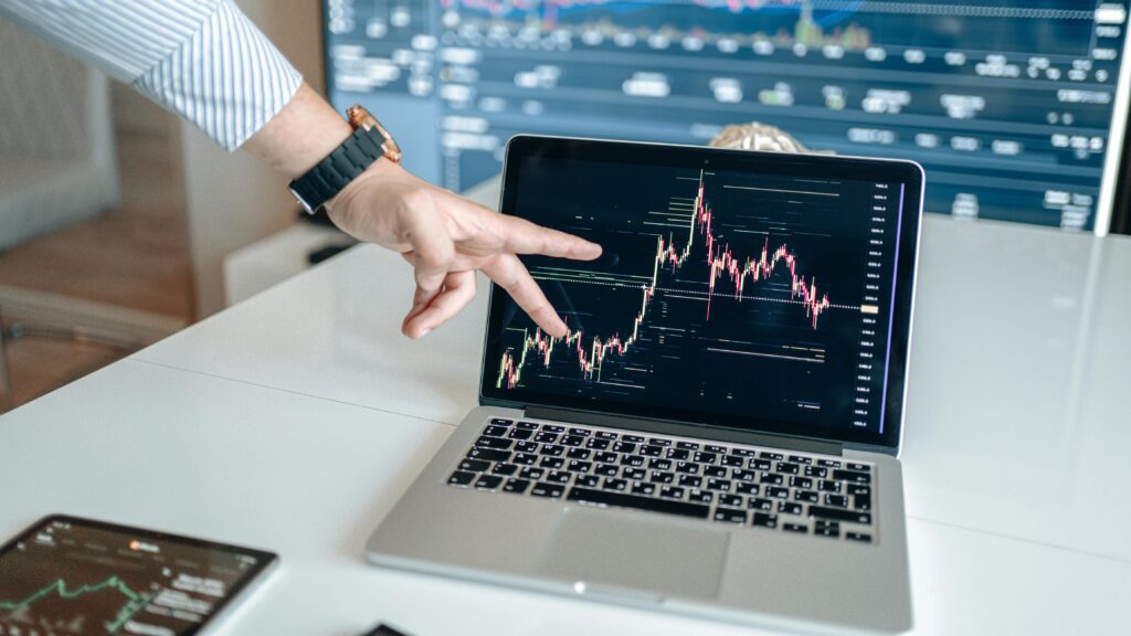 A person pointing at a laptop displaying a cryptocurrency market chart, indicating data analysis.